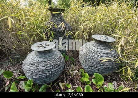 Des urnes en ardoise empilées (qui étaient des urnes du millénaire) exposées au château de Threave Gardens, à Douglas, avec un aménagement paysager de bambou doré et de Bergenia. Banque D'Images