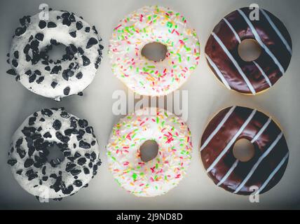 Flat Lay image de six beignets en anneau avec glaçure blanche et des centaines et milliers de couleurs, chocolat et rayures et glaçure blanche avec biscuits noirs Banque D'Images