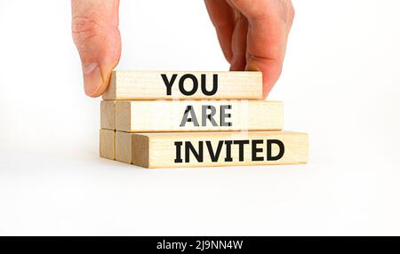 Vous êtes invité. Concept mots vous êtes invités sur des blocs de bois. Main d'homme d'affaires. Magnifique table blanche fond blanc. Et vous Banque D'Images