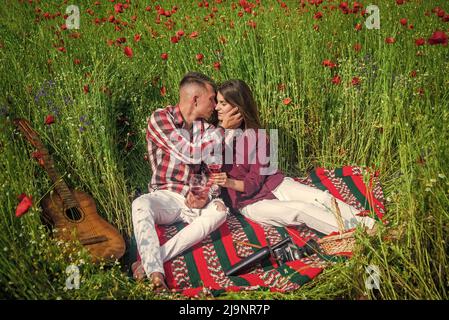 les amateurs de guitare boivent du vin dans le champ de fleurs. musique. couple amoureux. homme et femme dans le champ de pavot. Banque D'Images