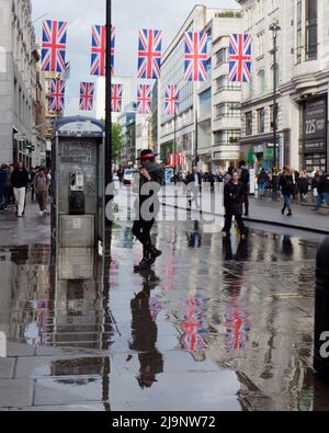 Londres, Grand Londres, Angleterre, mai 11 2022 : piétons dans Oxford Street après de fortes pluies avec Union Jacks reflétés dans l'eau. Banque D'Images