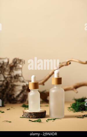 Flacons compte-gouttes en verre transparent avec sérum naturel. Branche d'arbre, écorce de bouleau, mousse sur fond. Banque D'Images
