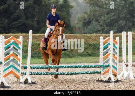 Une jeune femme jockey sur un cheval bondissant sur un obstacle. Banque D'Images