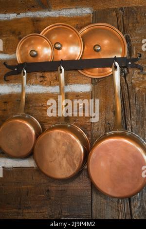 Gros plan de casseroles anciennes en cuivre et couvercles sur le mur de la cuisine à l'intérieur de la maison ancienne reconstruite en bois de 1800s. Banque D'Images