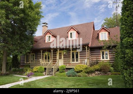 Réplique de l'ancienne maison en rondins de style cottage Canadiana 1800s avec cour avant paysagée en été. Banque D'Images