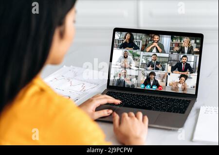 Vidéo conférence en ligne, brainstorming de groupe. Vue sur l'épaule d'une fille sur un écran d'ordinateur portable avec un groupe de gens d'affaires multiraciaux parlant sur un appel vidéo, discutant projet d'affaires, plan d'affaires Banque D'Images