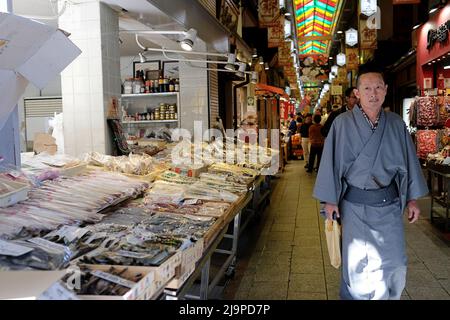 Un Japonais dans un yukata traditionnel passe devant un magasin de marchandises séchées sur les marchés Nishiki à Kyoto, au Japon Banque D'Images