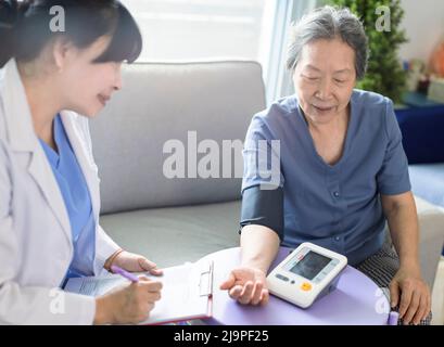 Un médecin soignant asiatique examine les patients âgés qui utilisent un manomètre de pression artérielle. Banque D'Images