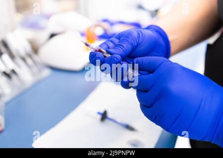 Les mains du dentiste préparent la seringue pour donner l'anesthésie dentaire à son patient. Mise au point sélective. Banque D'Images