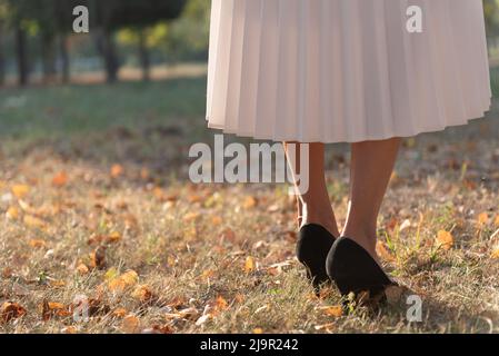 Coupe basse de femme dans une jupe blanche et talons hauts sur fond de parc flou. Banque D'Images