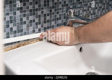 plombier enlever le vieux silicone de l'évier de salle de bains. Banque D'Images