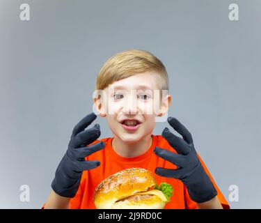 surpris garçon assis devant un énorme hamburger et montre ses mains portant des gants noirs Banque D'Images