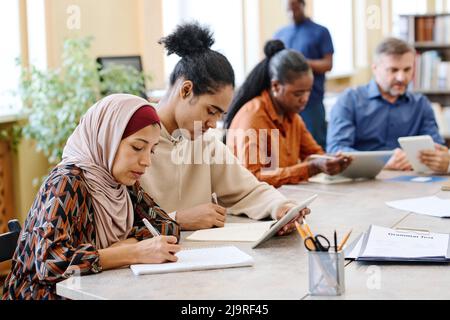 Groupe de personnes ethniquement diverses ayant des leçons de langue pour les immigrants assis à table faisant la tâche avec l'utilisation de tablettes numériques Banque D'Images