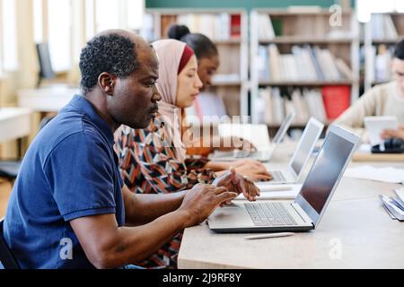 Groupe d'étudiants immigrants de diverses origines ethniques qui se sont envolés sur des ordinateurs portables pendant la leçon à la recherche d'informations sur Internet Banque D'Images