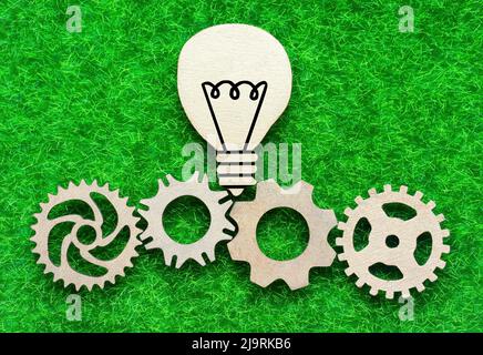 Ampoule plate en bois et roues dentées disposées sur un fond d'herbe verte. Ressources énergétiques écologiques alternatives et concept d'entreprise responsable. Banque D'Images