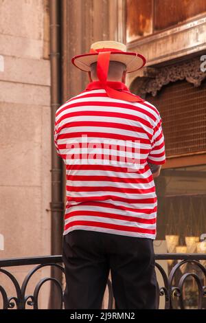 Italie, Venise. Chauffeur de gondole avec chemise à rayures rouges et blanches et chapeau avec ruban rouge. Banque D'Images