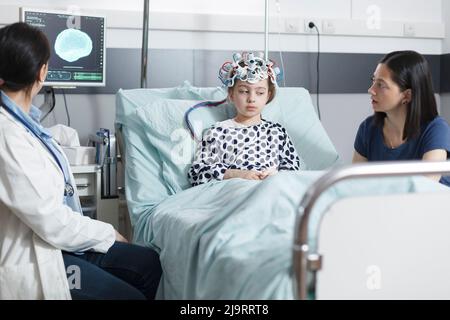 Hôpital de soins de santé pédiatrique medic analyse l'acquisition EEG de la petite fille mal en salle de réveil pédiatrique. Enfant patient portant un casque d'électroencéphalographie en clinique pédiatrique. Banque D'Images