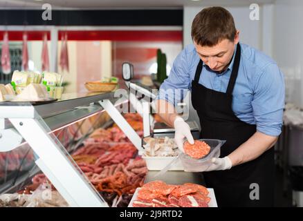 Smiling butcher debout dans une boucherie avec bac de matières premières fraîches escalopes steak de viande Banque D'Images