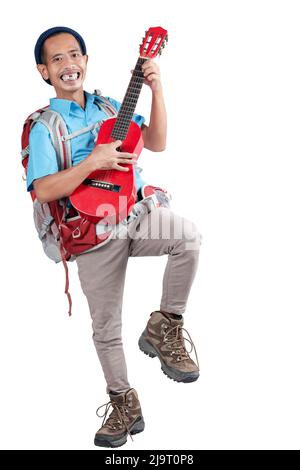 Homme asiatique avec un bonnet beanie et un sac à dos portant une guitare debout isolée sur fond blanc Banque D'Images