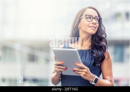 Femme d'affaires en lunettes a l'air debout à l'extérieur tenant une tablette. Banque D'Images