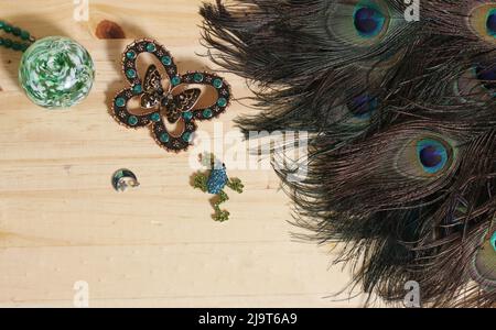 Plumes de paon avec perles vertes et brocher de papillons de cuivre et de vert sur table en bois Banque D'Images