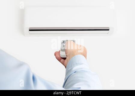 Un homme pointant une télécommande vers un climatiseur. Activation du chauffage ou du ventilateur Banque D'Images