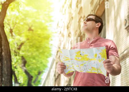 Touriste caucasien avec des lunettes sur la rue tenant une carte de la ville pour s'orienter Banque D'Images