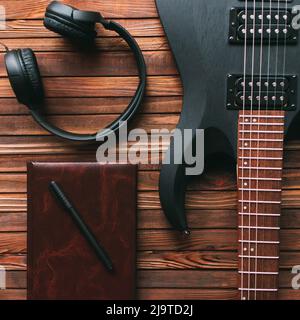Guitare électrique noire, bloc-notes et écouteurs sur une table en bois. Vue de dessus. Concept de création de musique. Banque D'Images