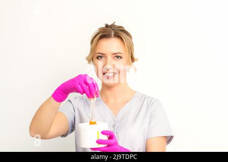 Portrait d'une esthéticienne caucasienne tenant un pot de pâte de sucre pour sugarer portant des gants roses sur fond blanc Banque D'Images