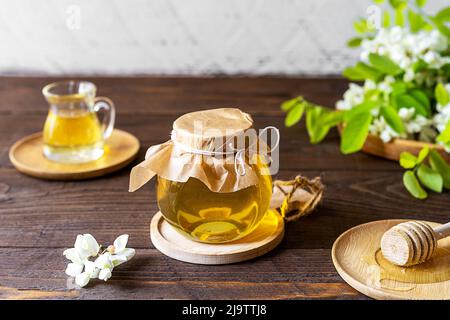 Miel d'acacia dans un pot en verre avec des fleurs de côté sur fond de bois Banque D'Images