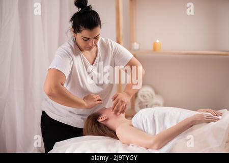 belle jeune femme ayant un massage du visage ou de la tête dans le salon de spa, masseuse faisant un massage du visage, les personnes et la relaxation spa Banque D'Images