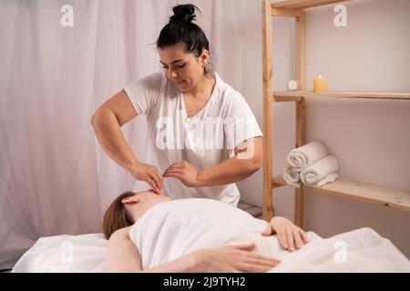 Masseuse faisant un massage visage et tête de jeune femme dans le salon de spa, soins de la peau et beauté Banque D'Images