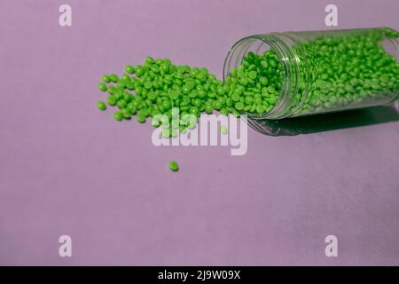 De magnifiques granules de cire verte avec extrait d'aloès pour l'épilation sont versés sur un fond violet clair, à partir d'un pot transparent. Épilation, épilation Banque D'Images