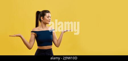 Femme souriante debout sur les genoux, en gardant les mains à l'intérieur. Vue portrait d'une jeune fille gracieuse en haut noir agenouillé avec les bras pliés aux coudes, isolé sur fond orange studio. Concept de pose. Banque D'Images