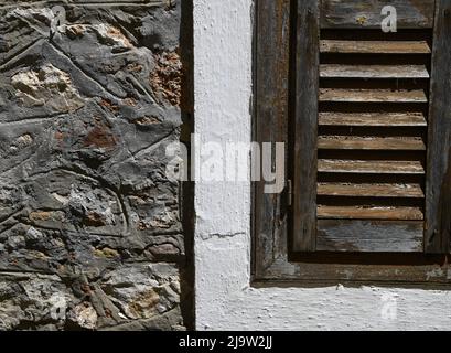 Ancienne maison rurale traditionnelle brun volets de fenêtre en bois avec garniture blanche contre un mur en pierre fait à la main. Banque D'Images