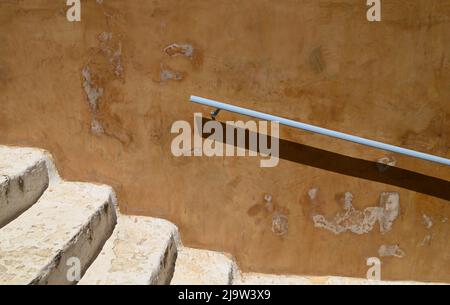 Des marches en pierre blanchie à la chaux, anciennes, sont posées contre un mur en plâtre vénitien ancien doté d'une main courante en fer bleu clair. Banque D'Images