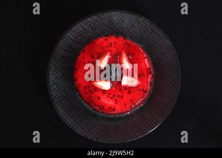 Un gâteau rond à la fraise dans un plat avec une mûre au milieu. Vue de dessus et sur fond noir. Ambiance sombre Banque D'Images