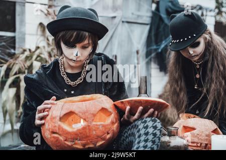 Petites filles effrayantes, sœurs célébrant halloween. Citrouille jack-o-lanterne.maquillage terrifiant visage noir, costumes de sorcière, image élégante.Horror, amusement à chil Banque D'Images