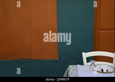 Cette taverne grecque traditionnelle dispose d''une table en verre, d''une assiette, de couverts et d''une chaise en osier en bois blanc placée contre un mur en bois. Banque D'Images