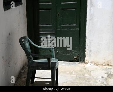 Ancienne maison rurale traditionnelle, porte en bois vert cyprès et chaise en plastique assortie contre un mur blanchi à la chaux. Banque D'Images