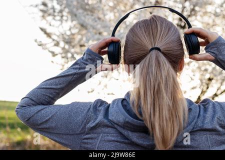 Femme avec un casque sans fil pour écouter de la musique à l'extérieur. Femme se détendant et appréciant la nature du printemps Banque D'Images