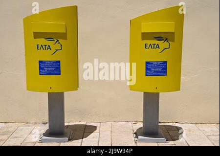 Boîtes aux lettres jaunes publiques de la poste grecque avec logos bleus et panneaux d'information contre un mur en stuc ocre à Nafplio, Argolis Péloponnese, Grèce. Banque D'Images