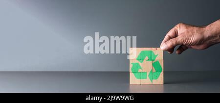 main posant des blocs de bois avec le symbole de recyclage avec fond gris et espace de copie, journée mondiale de la terre et journée mondiale de l'environnement . Banque D'Images