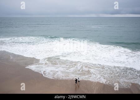 Les marcheurs de surf de plage s'humidifier dans les eaux côtières du golfe de Gascogne, le 12th mai 2022, à Comillas, Cantabrie, Espagne. Banque D'Images