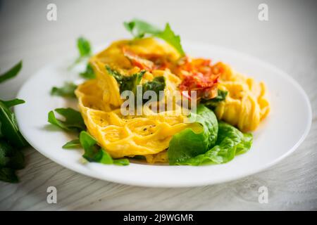 Omelette aux œufs farcie à la tomate et aux légumes verts frits sous forme de gaufres, sur une table en bois. Banque D'Images