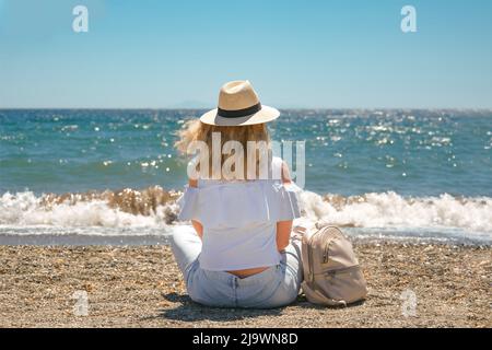 Femme en chapeau de paille et jeans bleu marchant le long de la mer. Banque D'Images