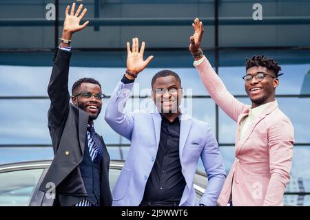 Un groupe de leurs trois hommes d'affaires afro-américains à succès dans un costume élégant parlant et se réjouissant sur le fond de fenêtre de gratte-ciel de rue Banque D'Images