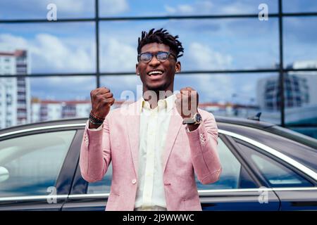 un homme d'affaires afro-américain heureux et réussi se réjouit et profite du succès devant la voiture. concept d'une bonne affaire et victoire Banque D'Images