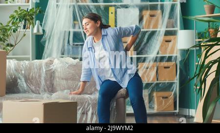 Une femme ressent une douleur soudaine au dos lorsqu'elle tente de soulever une boîte à carton. Banque D'Images