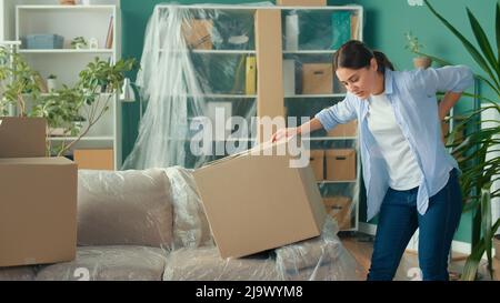 Une femme ressent une douleur soudaine au dos lorsqu'elle tente de soulever une boîte à carton. Banque D'Images